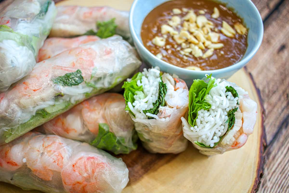 A mouth-watering photo of a bite-sized Goi Cuon spring roll, highlighting the vibrant colors of the fresh ingredients, including shrimp, lettuce, mint leaves, and rice noodles, wrapped in translucent rice paper.